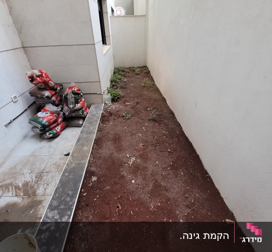 שקי אדמה וכלי גינון ליד ערוגת אדמה